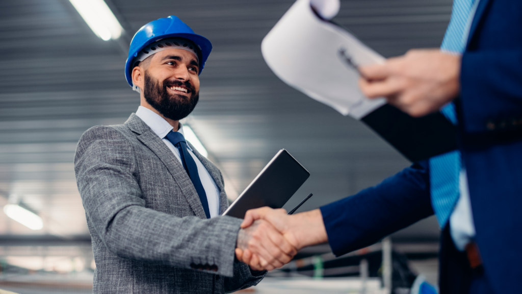 Man in suit and hard hat shaking hands with another man in the manufacturing factory