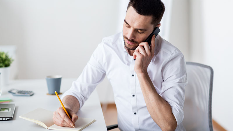 Person taking notes whilst listening to mobile phone