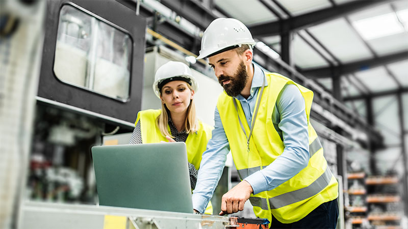 Two people in manufacturing setting working on computer